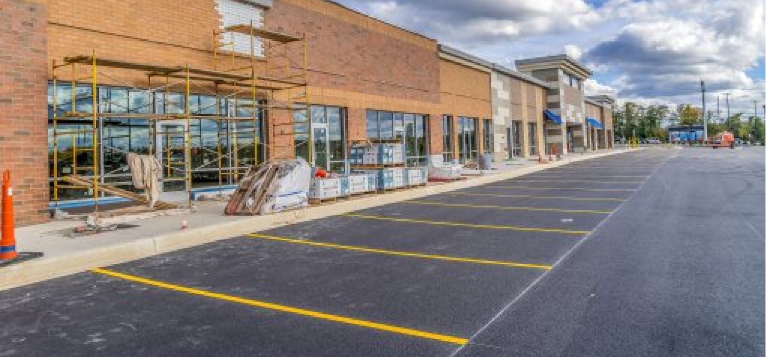 INVESTIRE IN IMMOBILI COMMERCIALI: CONSIGLI PER IMPRENDITORI 1 Centro commerciale in costruzione con ponteggi sulla facciata in mattoni, parcheggio asfaltato appena completato e materiali edili sul marciapiede