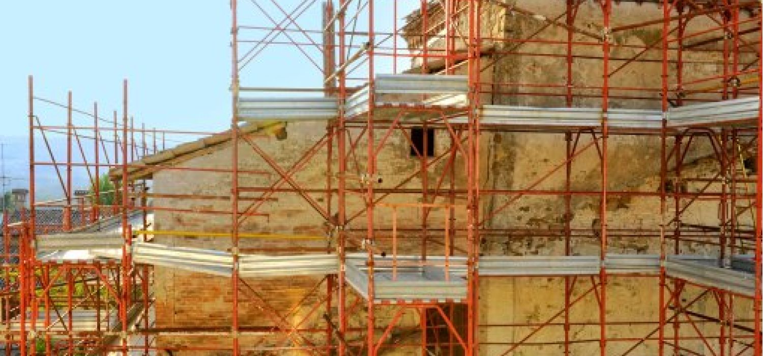 Ponteggio metallico rosso a più livelli attorno alla facciata in pietra di un edificio storico in fase di restauro
